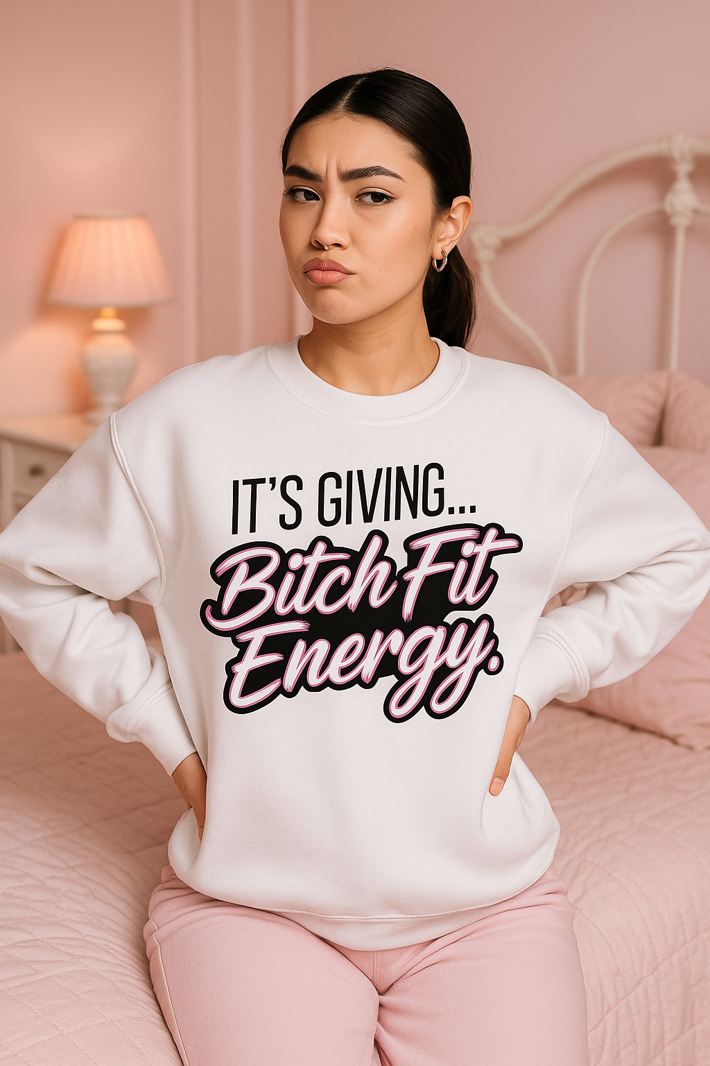 Woman wearing a white sweatshirt with text "Its Giving Bitch Fit Energy"     in a bedroom setting